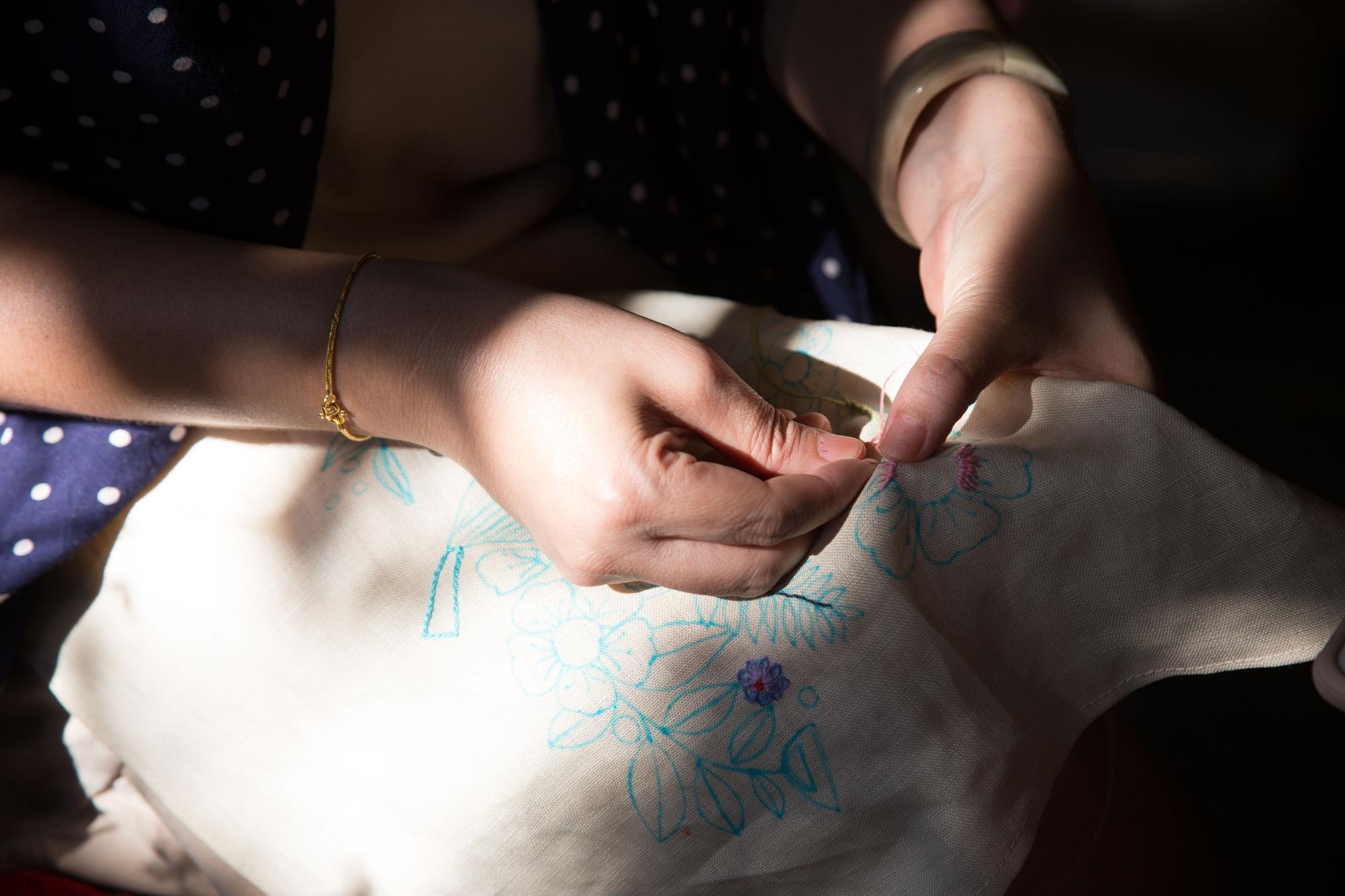Artisan hands threading needle over embroidered motif